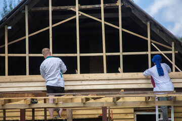 two builders reconstruct a wooden house, repairing a wall and a pediment
