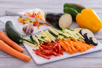 Fresh vegetables on a wooden table with a mix of sliced carrots, zucchini, courgettes, eggplant and peppers ready to be cooked - healthy eating vegetarian or vegan concept