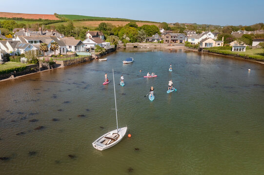 Aerial view of paddle boarders glide across the tranquil waters near the town, framed by quaint buildings and lush greenery, Kingsbridge, England, United Kingdom.