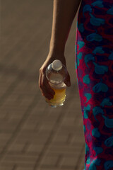A hand firmly grasps a colorful plastic water bottle, while the individual is dressed in a vibrant...
