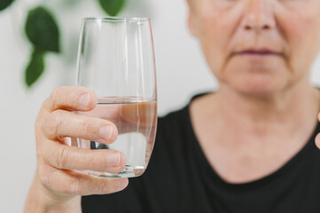 An elderly woman holds a glass of water in her hands.