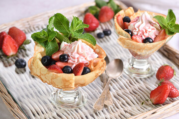 Cooking French pancakes with whipped cream filling with strawberries and blueberries, strawberry syrup, almond petals. Served in a glass and garnished with mint. 