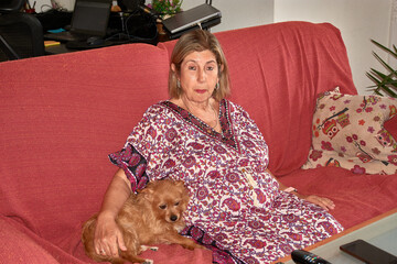 A quiet moment shared between an elderly woman and her reddish dog on a living room sofa decorated...