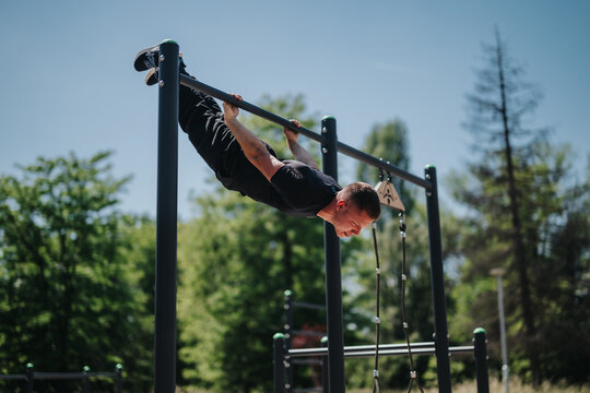 A man performing an advanced calisthenics move on parallel bars outdoors, showing strength and balance. The sunny park setting emphasizes physical activity, and motivation.