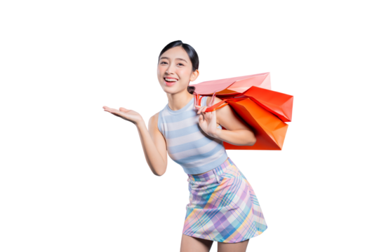 A cheerful young Asian woman with shopping bags, making a presenting gesture with her open hand to showcase a product or sale.on png
