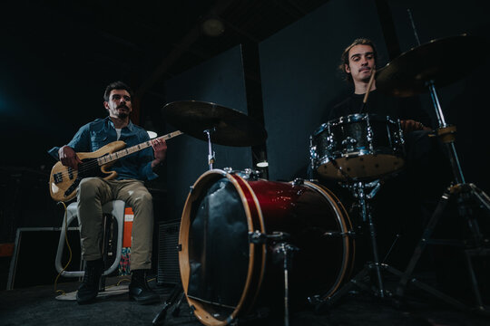 A band rehearsing in a moody studio with a bassist and drummer preparing for a performance.