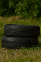 Two tires are carefully stacked on top of each other, resting on the green grass surface, creating an interesting visual arrangement