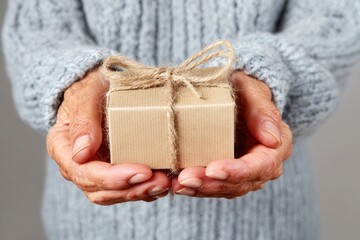 Elderly hands holding small gift wrapped in brown paper