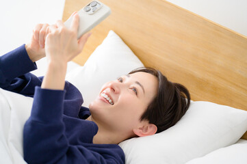 ベッドで仰向けでスマホを操作する日本人女性