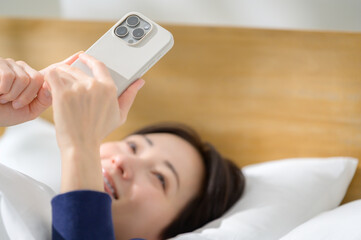 A Japanese woman operating her smartphone on her back in bed