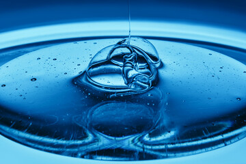 The viscous gel serum for the face flows and collects into a drop on a blue background..