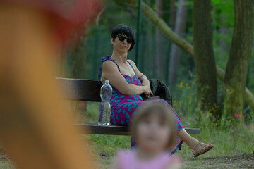 A woman is peacefully sitting on a lovely park bench, enjoying the moment while holding a bottle of...