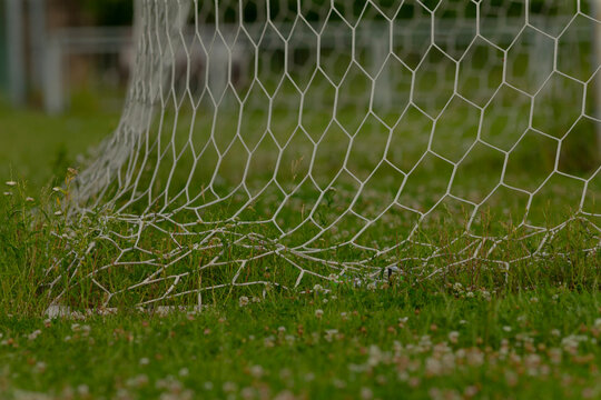 Here is a close up view of a soccer goal net situated on a grassy field. The netting is made of durable mesh, ready for game play