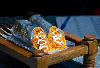 Close-up of freshly prepared shawarma or burrito wrap cut in half and served in aluminum foil on...