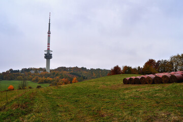 Meadow with Hay Bales and TV Tower beneath Overcast Sky