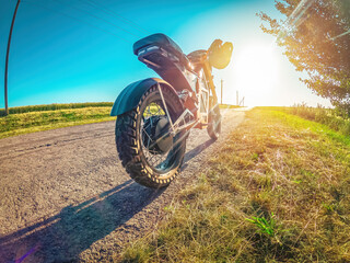 Electric motorcycle on side of road, standing near tree. Moped modern personal transport. Sunset.