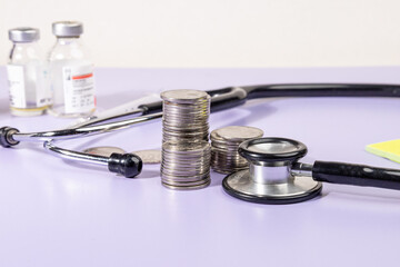 Stacks of coins alongside a stethoscope rest on a desk, symbolizing the financial burden and...