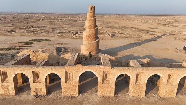 Historic view of Abu Dulaf Mosque in Samarra, Iraq, featuring its iconic spiral minaret and vast Abbasid-era architecture surrounded by desert landscape.