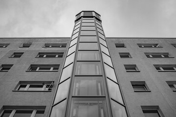 apartment building, high glass elevator shaft outside the house goes up into perspective. Above the house the sky is in clouds
