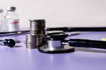 Stacks of coins alongside a stethoscope rest on a desk, symbolizing the financial burden and...