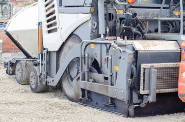 Construction workers in high-visibility gear are applyin gfresh hot asphalt to roadway surface