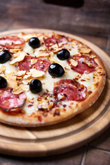 Pizza with salami, mozzarella and cheddar cheese. Wooden background. Soft focus. Close up.	