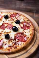 Pizza with salami, mozzarella and cheddar cheese. Wooden background. Soft focus. Close up.	