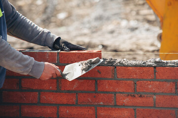 Bricklayer constructing stone wall using bricks, cement mortar mix and trowel