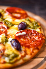 Pizza with chorizo ​​sausage, mozzarella and cheddar cheese, olive pesto and kalamata olives. Wooden background. Soft focus. Close up.	