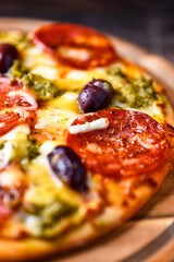 Pizza with chorizo ​​sausage, mozzarella and cheddar cheese, olive pesto and kalamata olives. Wooden background. Soft focus. Close up.	