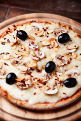 Pizza with champignons, black olives and mozzarella cheese. Wooden background. Soft focus.	