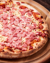 Pizza with ham and mozzarella cheese on wooden background. Soft focus. Close up	