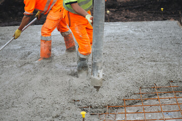 Construction worker operating a concrete pump at a job site in the daytime, focusing on the pouring process and surrounding activity