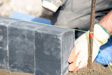 Close-up of bricklayer carefully placing black paving bricks on  prepared base at construction site