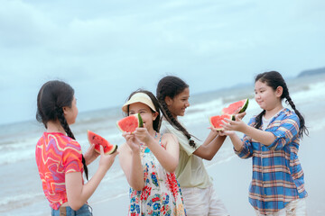 Friends enjoying watermelon slices at the beach during a sunny summer day