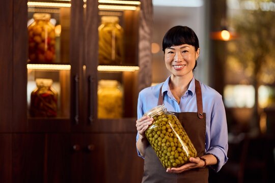 Smiling Woman Holding Jar of Pickled Olives in a Cozy Store Setting