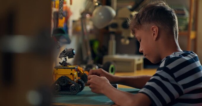 A boy enthusiastically builds a robot from a construction kit while sitting at a table at home