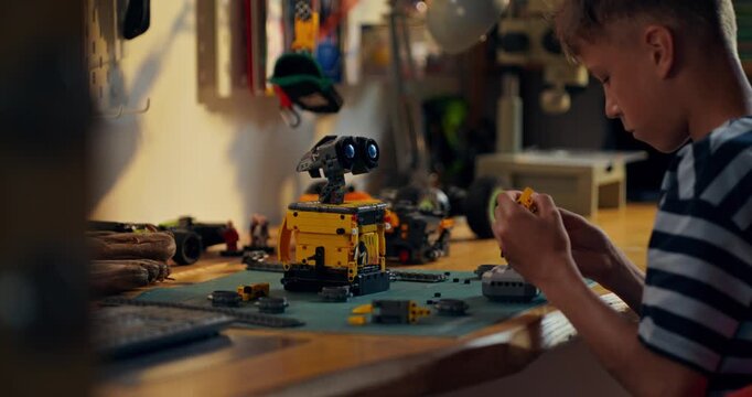 A boy is concentrating on building a robot from a construction kit while sitting at a table in his room