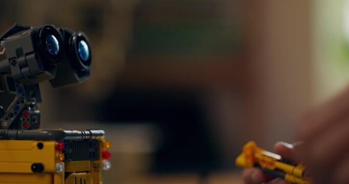 A boy builds a robot from a construction kit while sitting at a table at home. Close-up of his hands, unrecognizable person