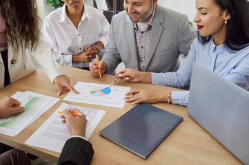 Diverse group of professionals around table in office, reviewing documents, charts, discussion,...