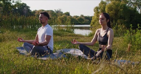 Family couple meditates in lotus position during yoga session near lake in forest, boosting outdoor training, crafting a serene space where workout and relaxation blend with nature tranquil embrace. - Powered by Adobe