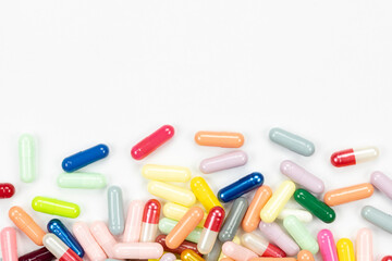 Scattered colorful medicine capsules and pills creating a bottom border with copy space for text, isolated on white background