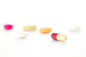 A single red and white medicine capsule in sharp focus against a blurred background of colorful...