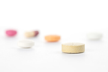Macro photo with selective focus on a single yellow pill, with other colorful tablets blurred in...