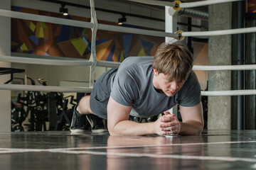 Young caucasian male person in gray sportswear does plank position at gym. Fitness center. Health...