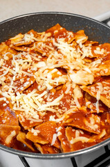 Chilaquiles with melted cheese and red sauce cooking in a pan