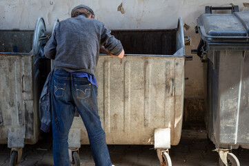 Individual rummages through a dumpster looking for valuable items or recyclables in an urban...