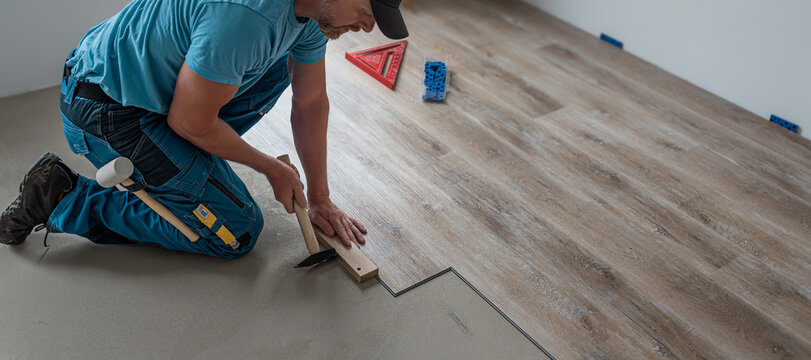 Floating floor work. The worker's hands taps the board of vinyl plank to lock the click system.