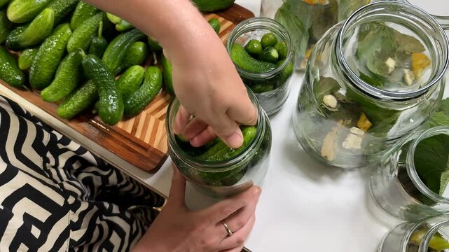 A person pickles cucumbers in jars, showcasing home preservation, fermentation, and culinary traditions with a focus on organic produce