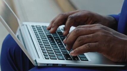 Crop view of African American employee hands write report on laptop sitting outdoors. Businessman types processing document online during break in urban environment closeup - Powered by Adobe